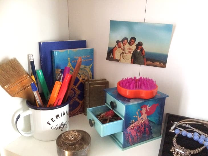 A desk filled with objects, including books, a mug of pens, and a Little mermaid jewelry box