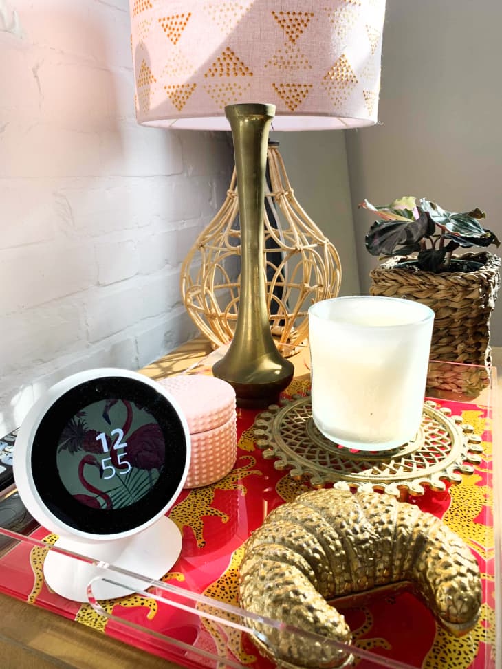 An Amazon Echo spot on a nightstand, surrounded by candles, a lamp, and other decorative objects