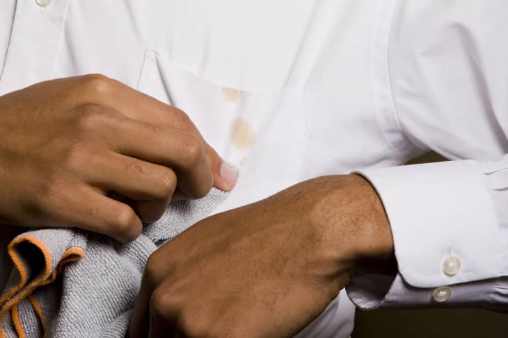 man using a gray towel to blot a brown-colored stain on a white button-up shirt
