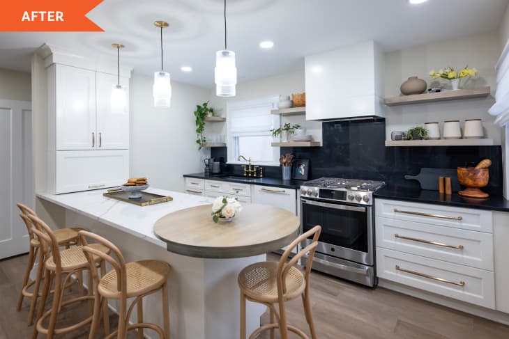 "after" photo of a white kitchen with black countertops, stainless steel oven/stove, gold hardware on drawers and sink faucet. Kitchen island with rounded edge and cane/rattan barstools. 3 overhead pendant lamps