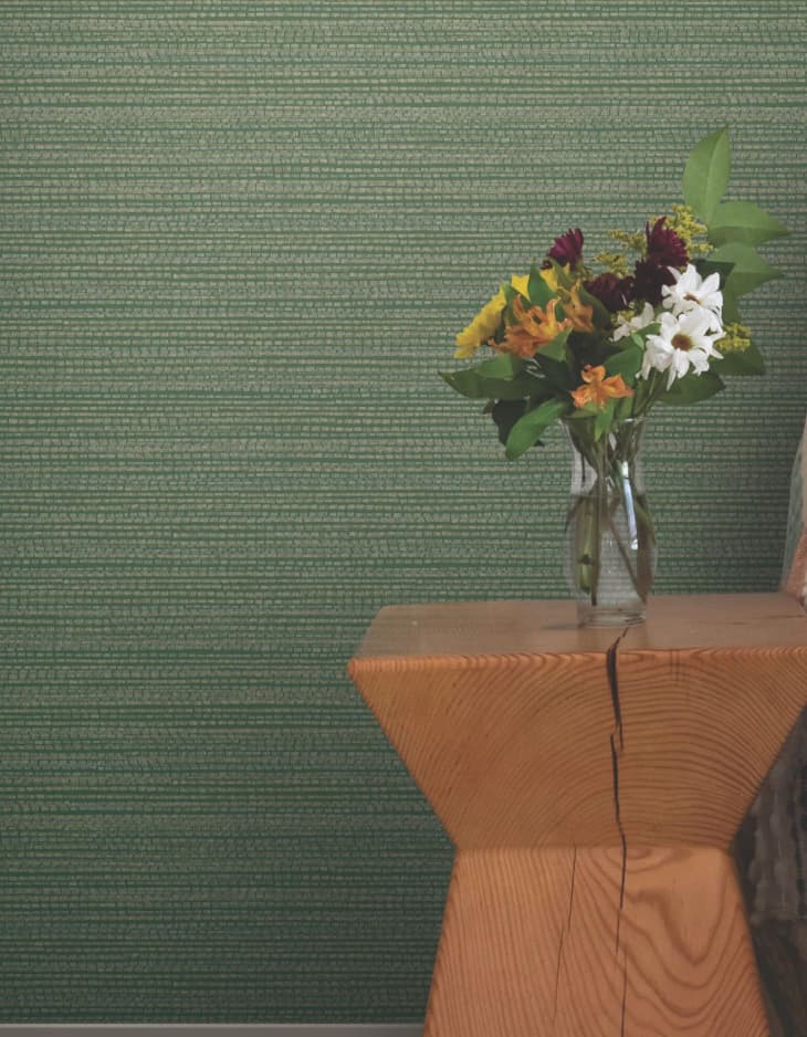 A textured green wallpaper behind a vase of flowers