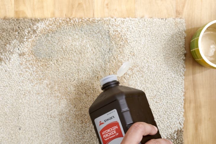 Overhead view of hydrogen peroxide being poured onto a coffee stain on a white and brown rug.