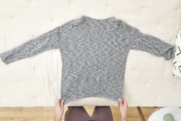 Overhead of a grey sweater laid out on a beige duvet.