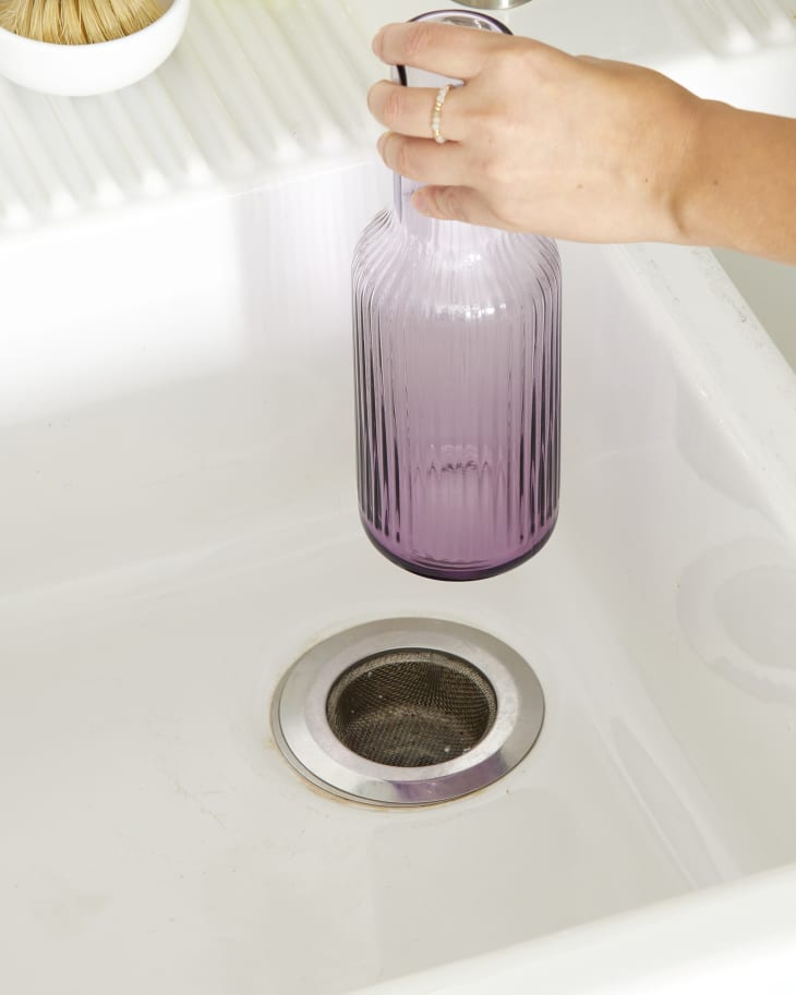 Angled view of a hand pulling up a purple vase on a sink drain.