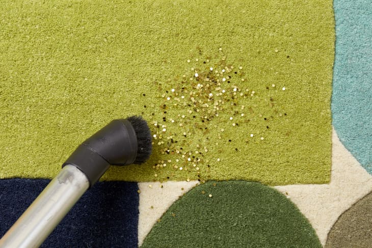Close up view of a vacuum brush cleaning up gold glitter from a multicolored carpet.