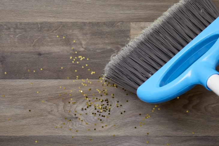 Close up of a broom sweeping up gold glitter off a  wood floor.
