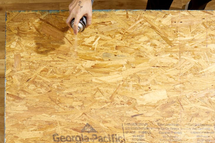 Close up shot of a hand spraying adhesive onto a large piece of plywood.