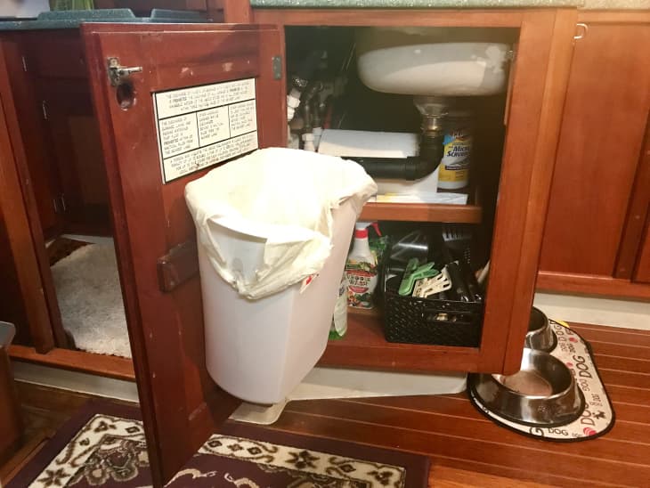 small white trash can hanging on inner door of sink cabinet