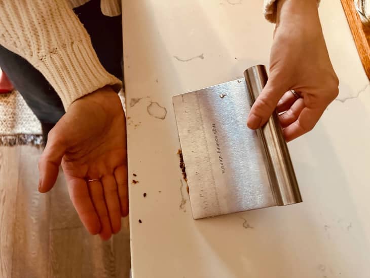 person using a bench scraper to move crumbs off counter into their hand