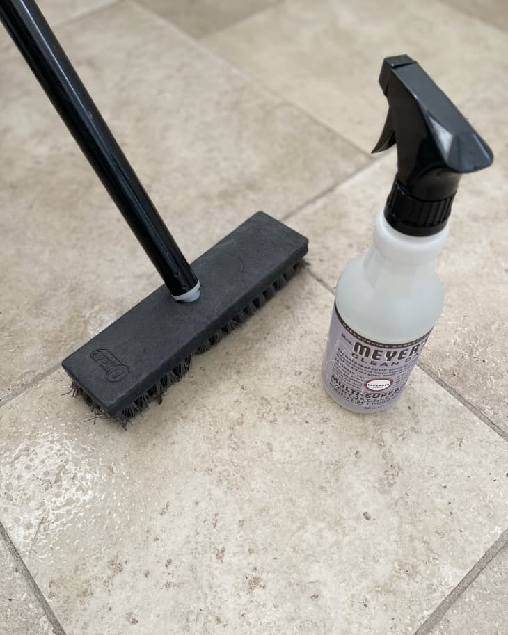 Someone using deck brush and all purpose cleaner to clean tile floors.