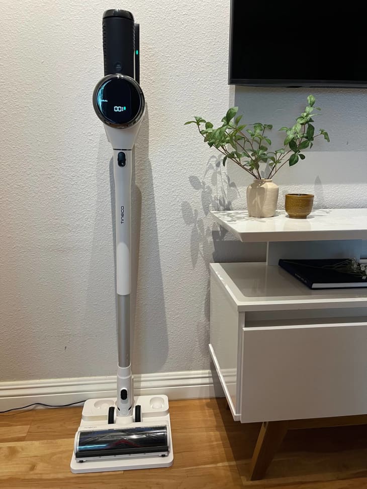 Tineco cordless vacuum leaning against wall next to a TV and TV console table