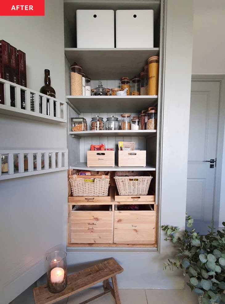 Pantry after makeover. Freshly painted doors, white bins on top shelf, things are organized and tidy. Theres a small wood stool and a plant on the floor