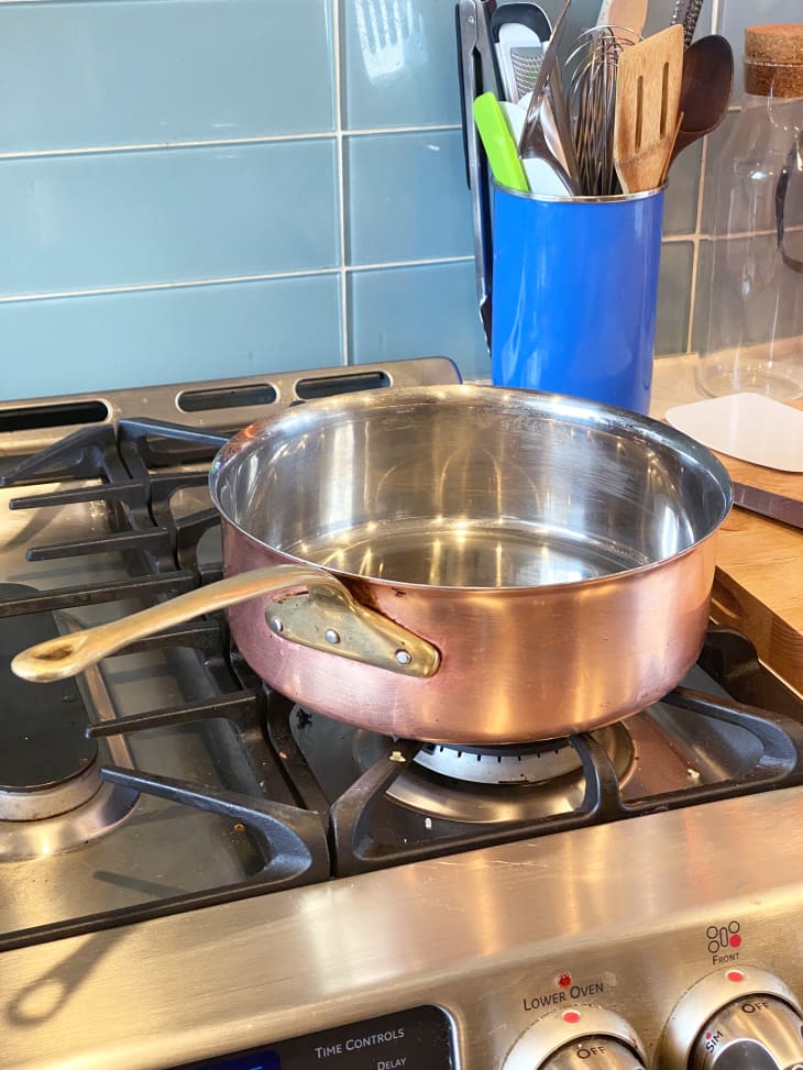 A shiny, clean copper pot sits on the front right burner of a gas stovetop.