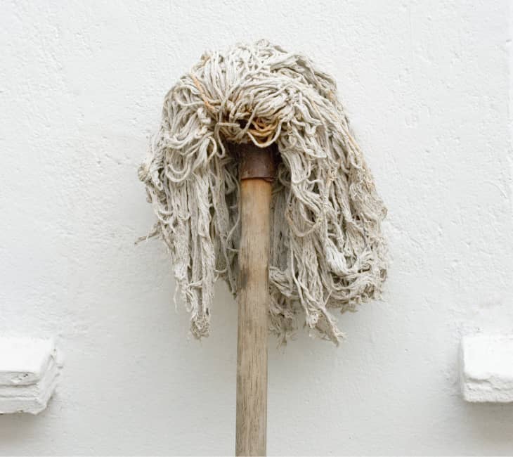 Old string mop resting against a white wall