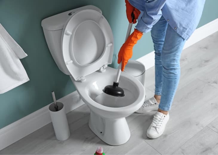 A woman unclogging a toilet incorrectly with a cup plunger