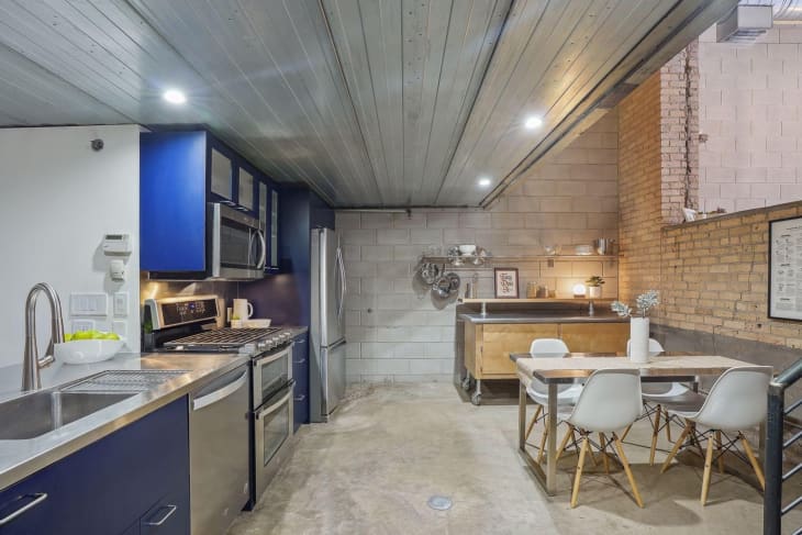 Kitchen in industrial loft--cinder block and brick walls, blue cabinets, other stainless steel, wood, and white accents
