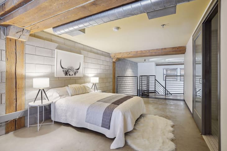 Bedroom in industrial loft. Minimal furnishings, cinder block wall, exposed structural beams