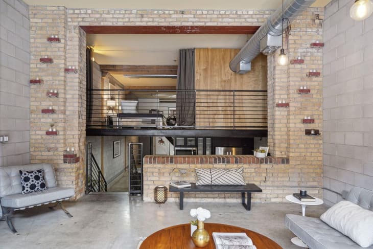 Living room in industrial loft. Cinder block and exposed brick walls, lots of light, minimal furnishings, staggered brick "shelves"