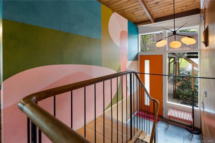 stairway area with mural/graphic painted on wall, orange front door, wood ceiling, windows