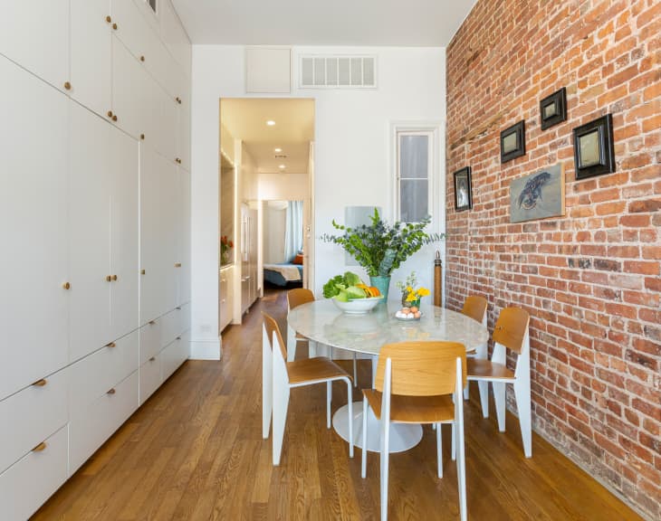 White dining room table in brick walled room with lots of cabinets.