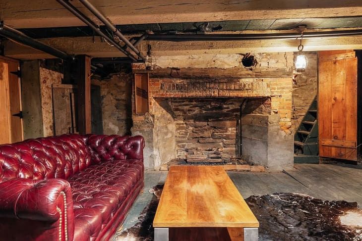 Red leather chesterfield sofa next to brick chimney in basement of historic home.