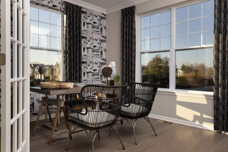 room with table with 2 chairs, laminate floor, large windows, black and white wallpaper accent wall
