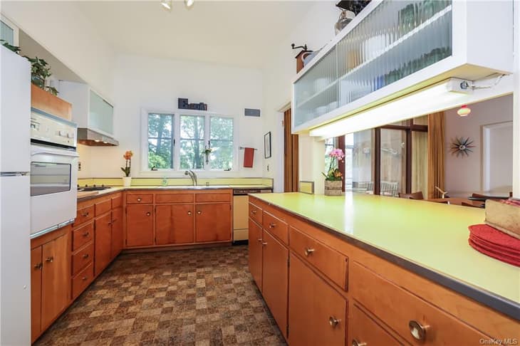 Green countertop in kitchen with wooden lower cabinets and fluted glass white upper cabinets in mid-century home.