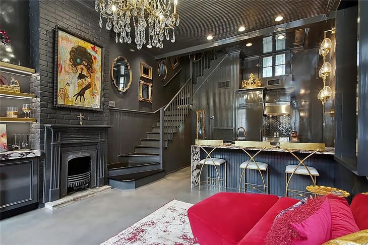 Kitchen and living room area of New Orleans home with black painted interior and colorful painting mounted over fireplace.