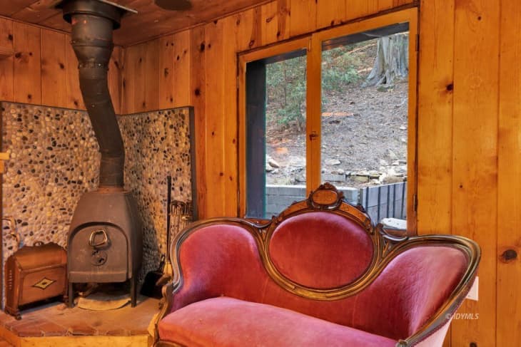 living room in cabin with wood burning stove, wood walls, and velvet queen anne or regency style velvet loveseat