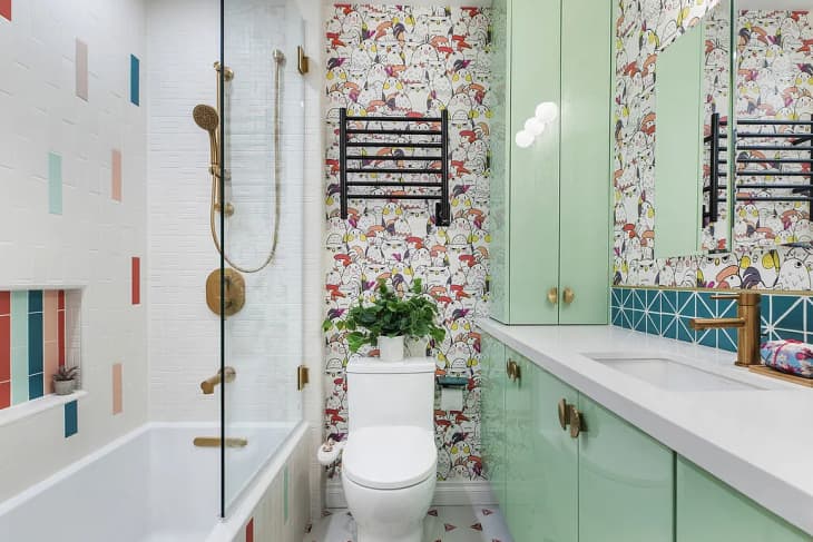 bathroom with colorful wallpaper, mint green cabinets, and white and colored tile block shower