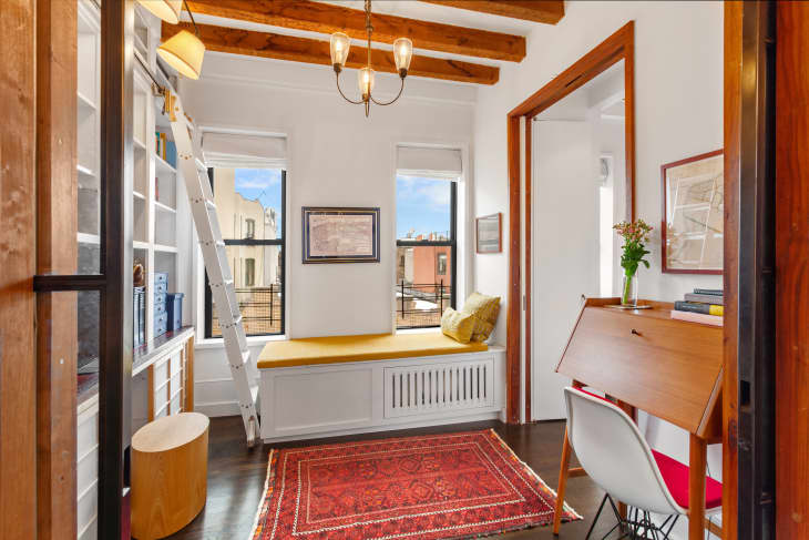 家庭办公室红色的复古地毯，嵌入式窗座椅与黄色厨房，中世纪书桌在角落，嵌入式书架与梯子