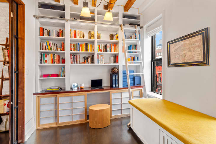 带黄色靠垫的嵌壁式长凳和带梯子的嵌壁式书架的家庭办公室