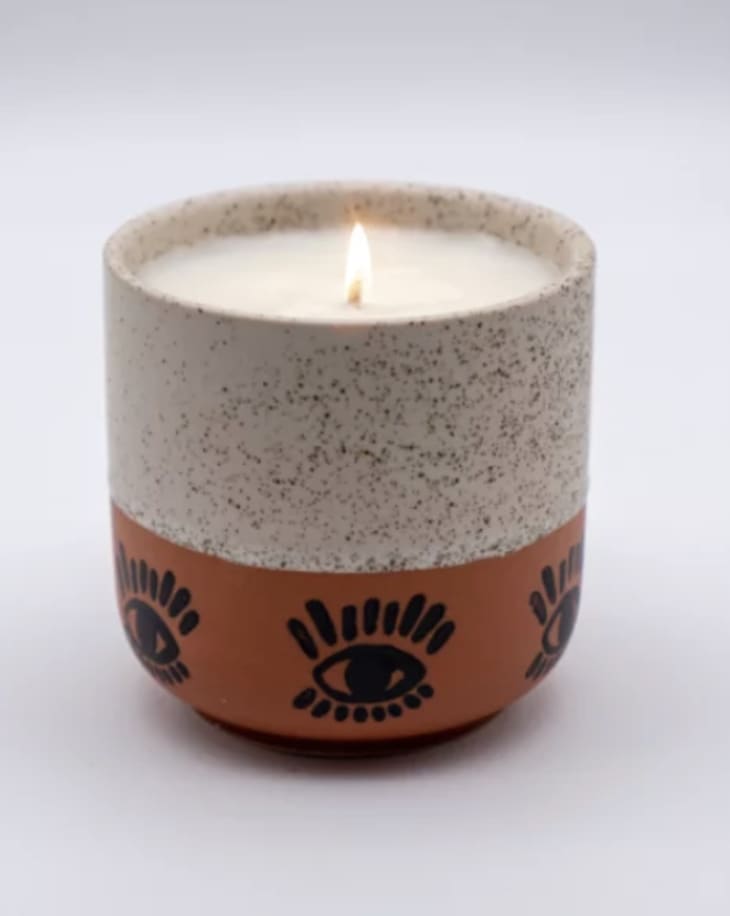 Lavender candle in a speckled terracotta vessel with an eye motif on it
