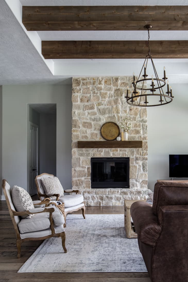 Living room with stone fireplace and rich dark wood beams by Moore House Interiors