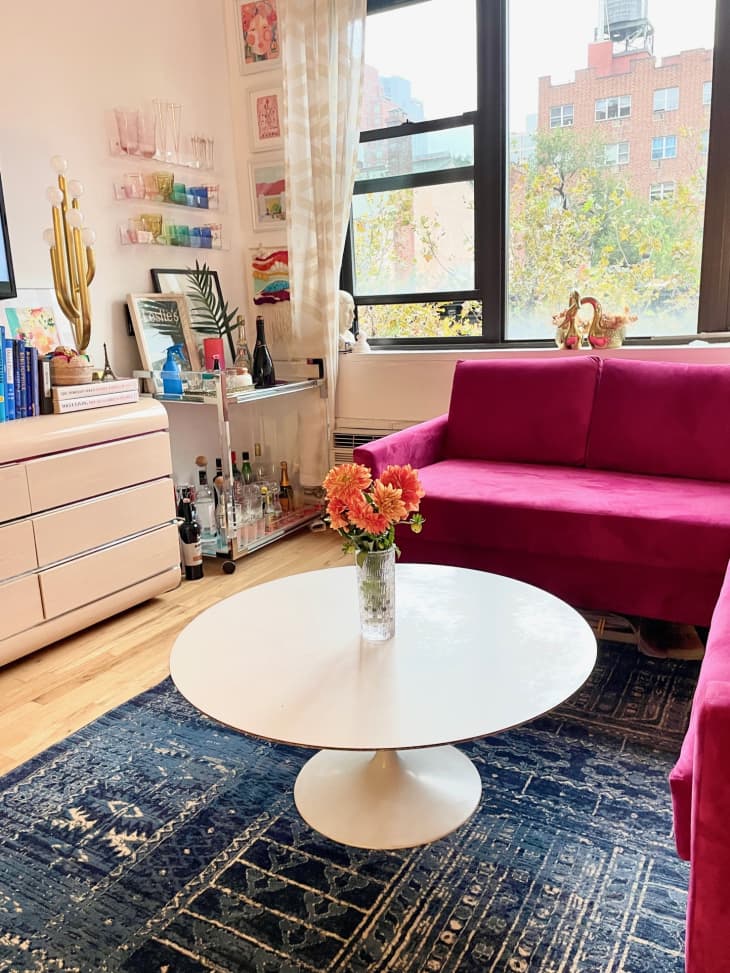 Hot pink sofa, blue rug, and a 1960's tulip table with a pink 80s dresser as a media cabinet in Erica Finamore's NYC apartment