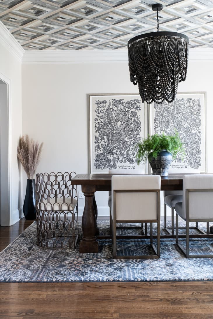 Dining room designed by Marie Cloud of Indigo Pruitt with a wallpapered ceiling, beaded black chandelier, wooden table, metal chairs, and a set of two tonal floral prints hanging on the wall