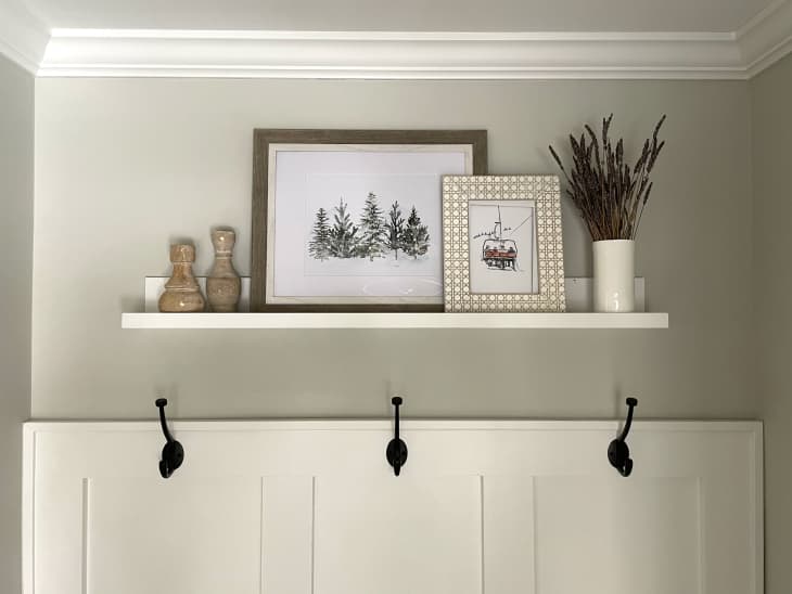 Ikea Mosslanda photo ledge hung in a entryway with  photos, dried lavender and other decorative objects on top.