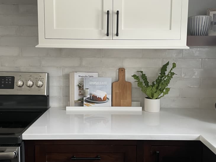 Ikea Mosslanda photo ledge in a kitchen with cookbooks and small cutting board on top.