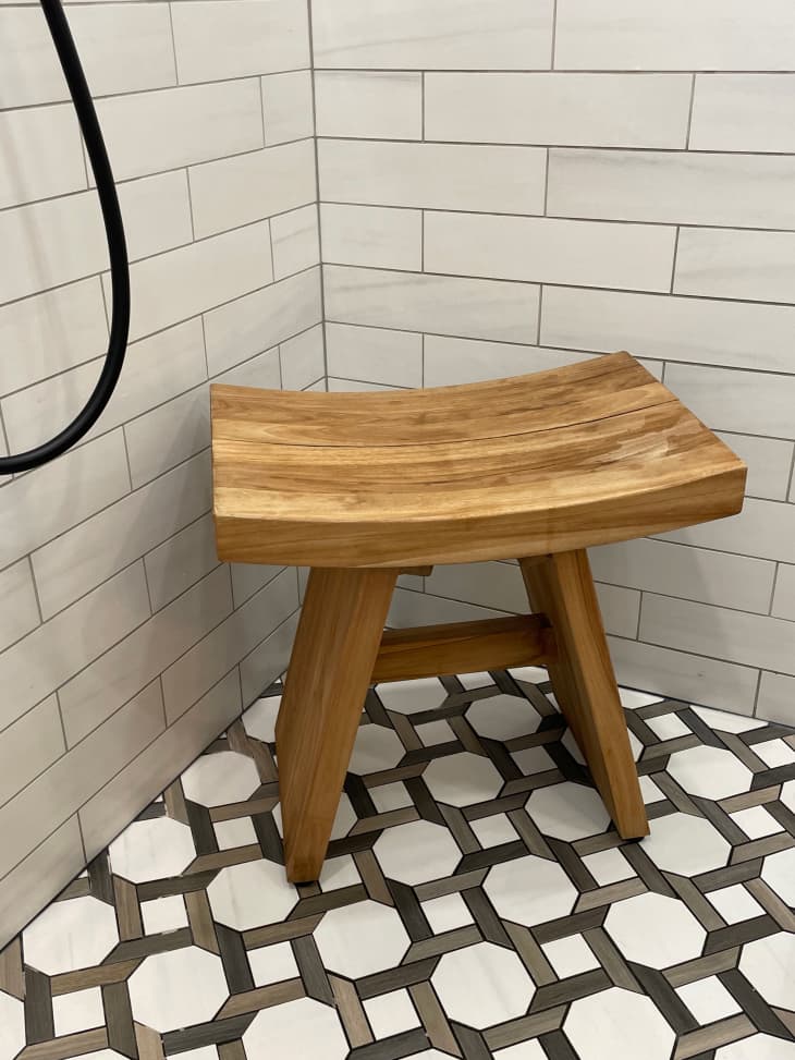 Wooden bench in newly renovated shower with black and white floor tiles and white subway tiles on the walls.