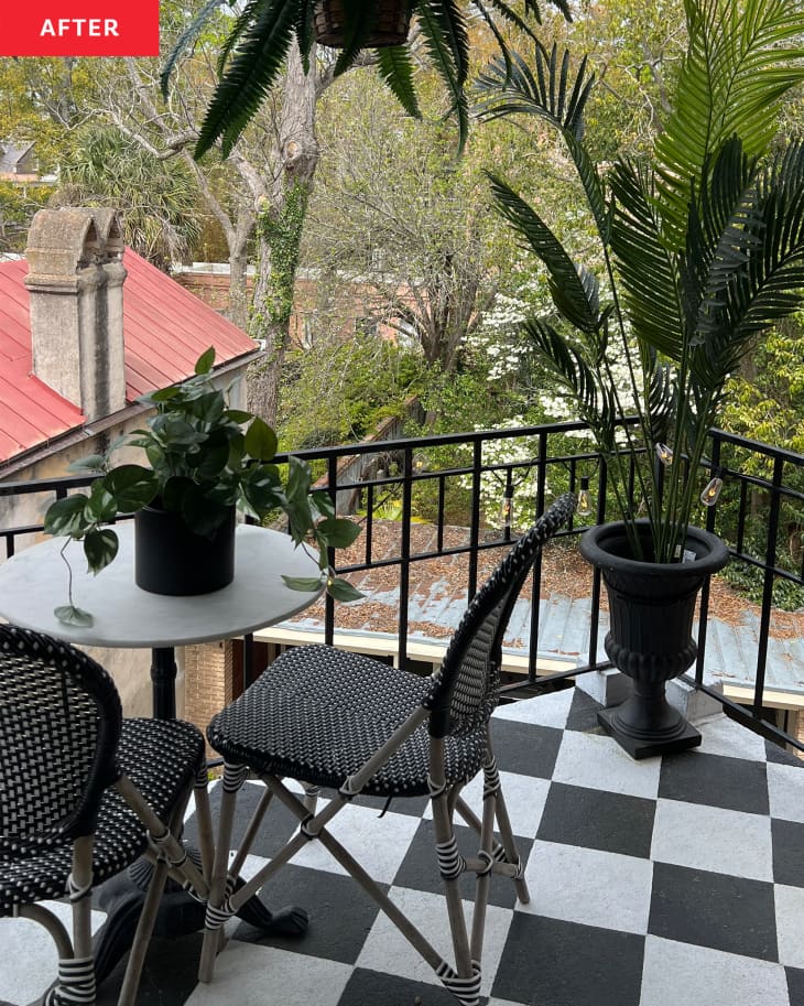 View of small terrace from living room after makeover. Black and white checkered painted floor, small round table with 2 woven chairs, plants in corners, 2 large ferns hanging