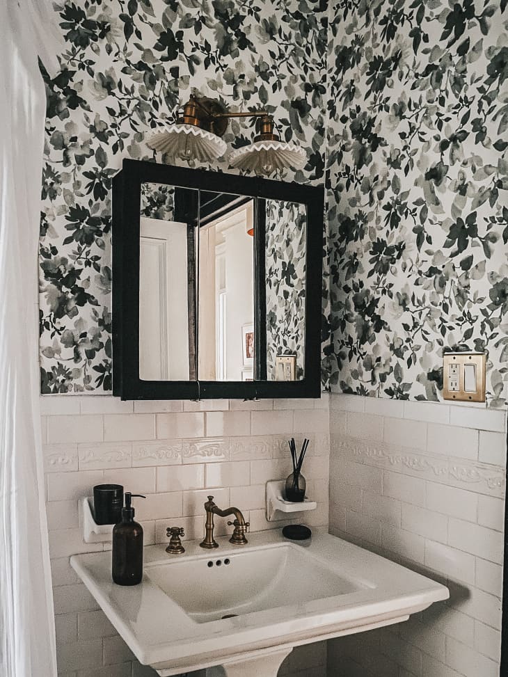 Vintage bathroom with white subway tiles,  floral wallpaper and scalloped lighting above medicine cabinet.