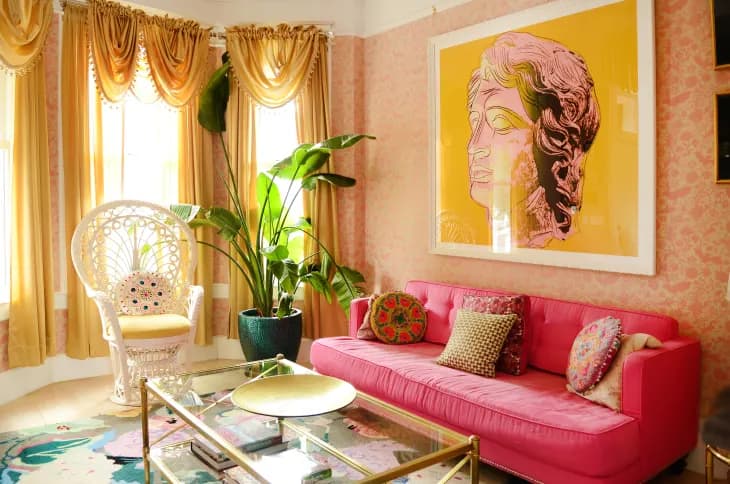 bright pink couch against a peach wall with yelllow wall art and curtains