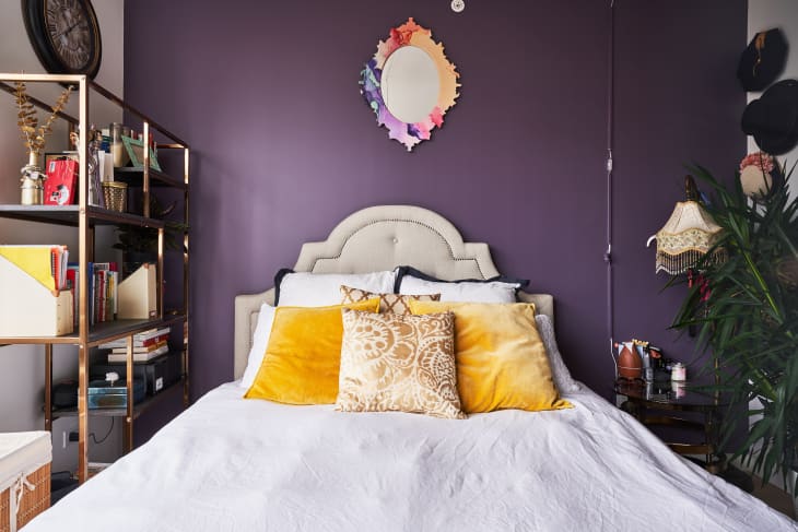 bed with a white duvet with yellow throw pillows against an eggplant purple wall