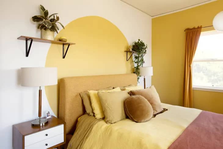 yellow bedding with orange pillows and a dusty rose throw blanket. yellow wall accents and orange curtains