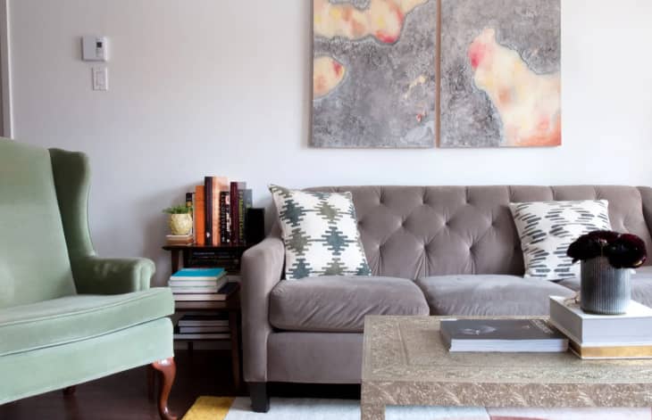 a gray couch with a tufted back next to a velvet mint green armchair