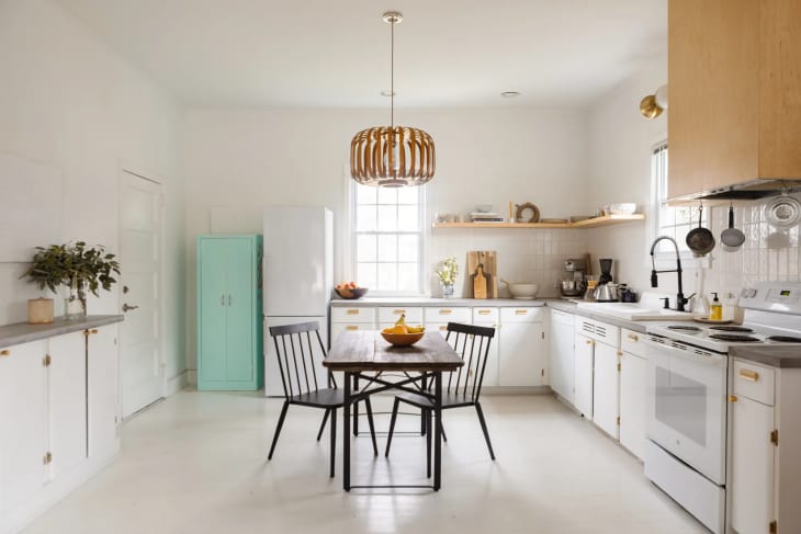 a white minimalist kitchen with a vintage mint green refrigerator and dark wood dining set