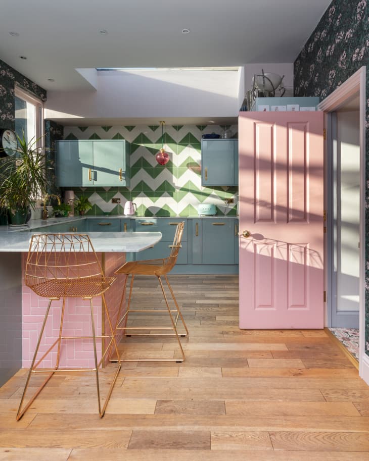 Emily Murray of The Pink House's kitchen with pastel pink doors and island, a white and green chevron wallpaper, and mint cabinetry