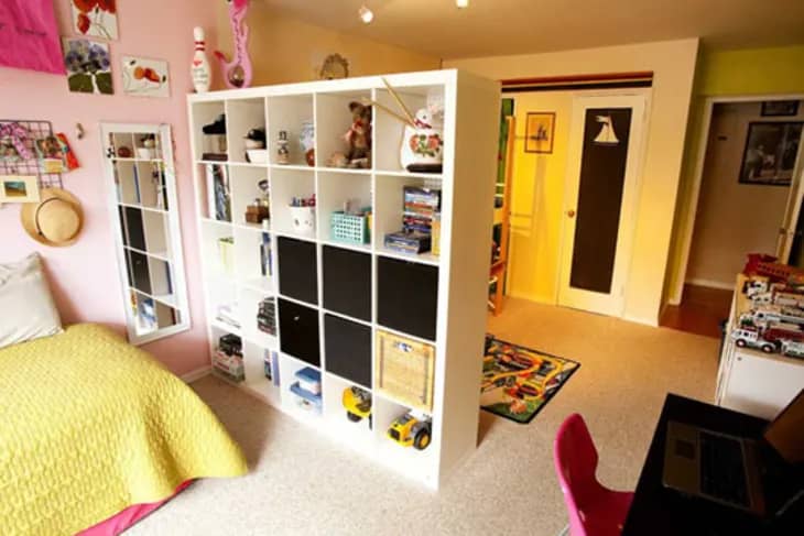 a kids' bedroom separated by a bookshelf filled with toys and children's book