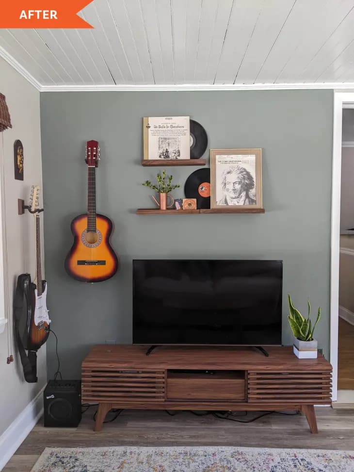a tv on a wooden stand with shelves and a mounted guitar on the wall behind it