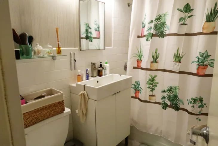 a white bathroom with white walls featuring a white shower curtain with a potted plant design